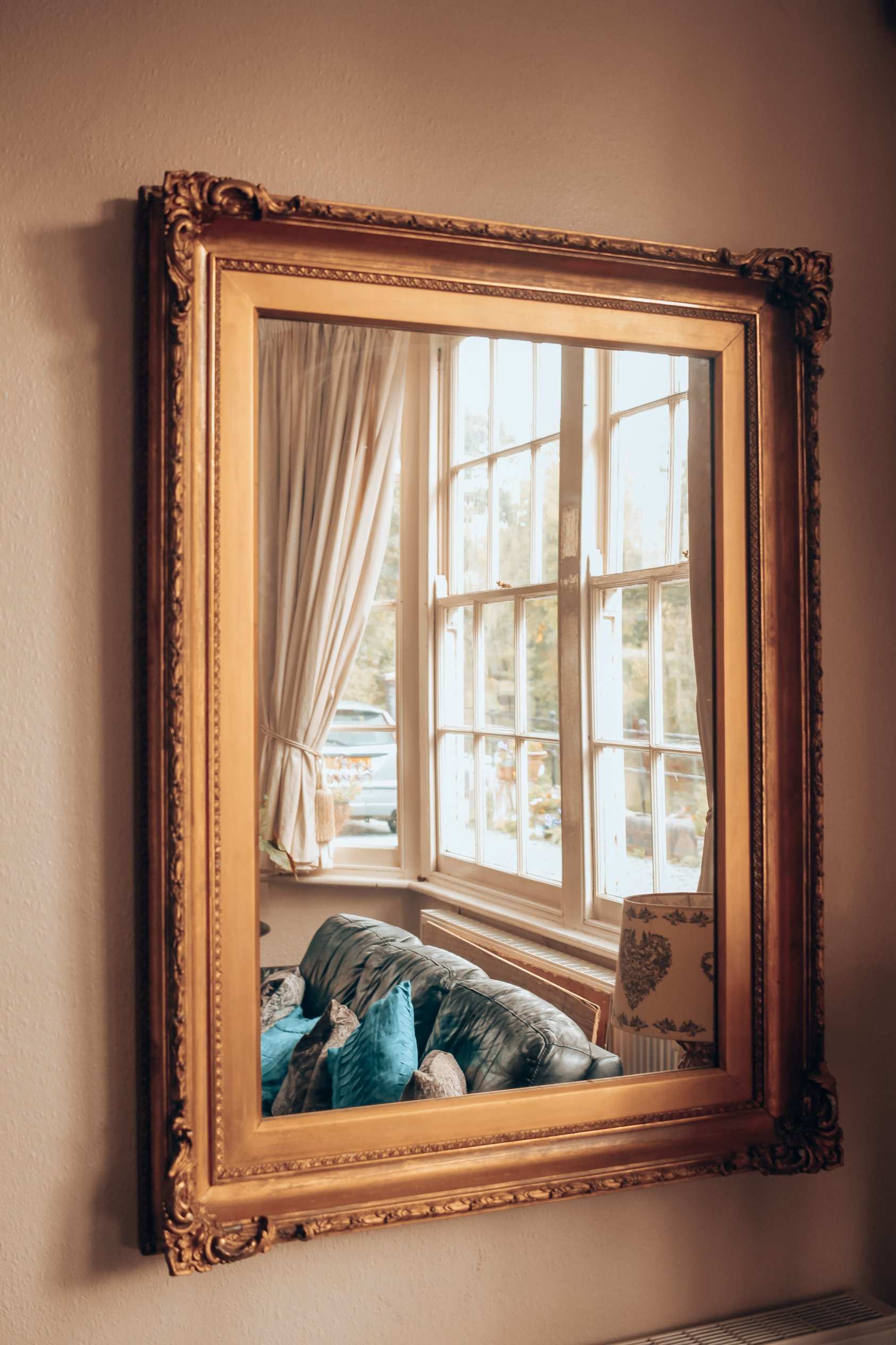 A gilt mirror reflecting a sofa and window