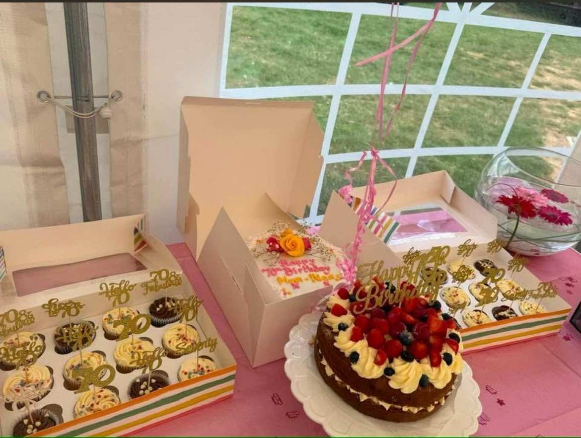 A birthday cake and boxes of cupcakes on a table in the marquee