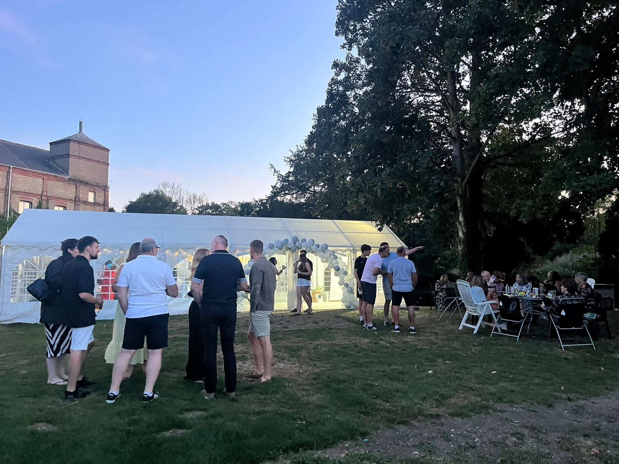 Guests gathered on the lawn outside the marquee on a summer evening, the old mill behind